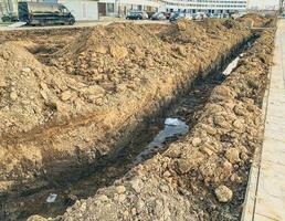 Sandgraben mit Kommunikation. Rohre werden in einem neuen Mikrobezirk der Stadt verlegt, um die Kommunikation zu Wohngebäuden zu bringen foto