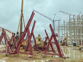 Baustelle eines Industriekomplexes. Rote Strukturen, die zur Absturzsicherung zusammengestapelt sind. lange Metallstöcke zum Bauen von Fundamenten und zum Verstärken von Gebäuden foto