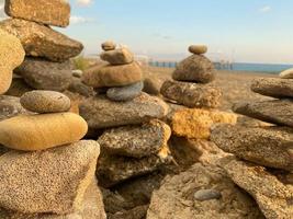 Eine Pyramide aus übereinander gestapelten Steinen am Strand und Sand mit kleinen natürlichen bunten Steinen am Ufer vor dem Hintergrund des Meeres bei Sonnenuntergang foto