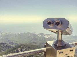 Fernglas auf einer Aussichtsplattform aus grauem Metall. Sightseeing-Tour, die Aussicht von den Bergen beobachten. Fernglas vor dem Hintergrund einer bergigen Ebene mit viel Grün foto