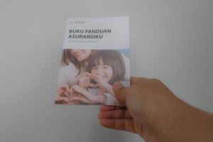 west java, indonesien im juli 2022. eine hand, die manulife's versicherungshandbuch für lebens- und krankenversicherungen hält foto