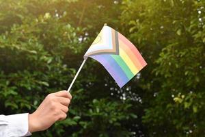 neue lgbtqai-flagge, die aus papier in der hand hält, konzept für lgbtqai-gemeinschaftsfeiern und respektieren der geschlechtsvielfalt auf der ganzen welt im stolzmonat, weicher und selektiver fokus.