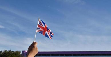 nationale flagge des vereinigten königreichs oder die union jack-flagge, die in der hand hält und auf blauem himmelshintergrund winkt, weicher und selektiver fokus.