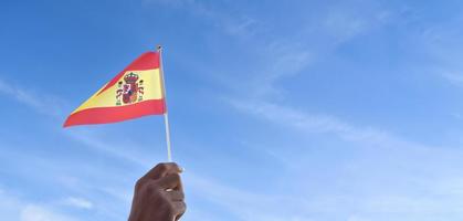 spanische nationalflagge oder spanien-flagge, die in der hand hält und auf blauem himmelshintergrund winkt, weicher und selektiver fokus. foto