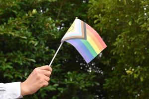 neue lgbtqai-flagge, die aus papier in der hand hält, konzept für lgbtqai-gemeinschaftsfeiern und respektieren der geschlechtsvielfalt auf der ganzen welt im stolzmonat, weicher und selektiver fokus.