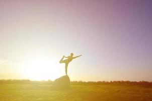 Silhouette eines jungen blonden Mädchens im Sportanzug Yoga auf einem malerischen grünen Hügel am Abend bei Sonnenuntergang. das konzept der übung und des gesunden lebensstils foto