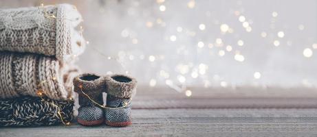 Stapel kuscheliger Winterstrickpullover und süßer kleiner Stiefel auf verschwommenem Hintergrund mit Bokeh. warmes gemütliches konzept. Banner-Image für Design foto