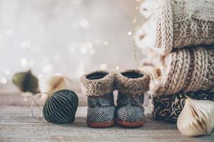 Stapel kuscheliger Winterstrickpullover, süßer kleiner Stiefel und Weihnachtsschmuck auf verschwommenem Hintergrund mit Bokeh. foto