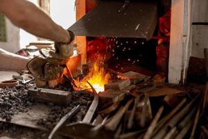 der Schmied im Produktionsprozess von Metallprodukten, handgefertigt in der Schmiede. Handwerker erhitzt Metall im Feuer. Metallindustrie, alter Beruf. foto