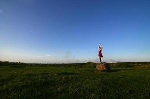 Silhouette eines jungen blonden Mädchens im Sportanzug Yoga auf einem malerischen grünen Hügel am Abend bei Sonnenuntergang. das konzept der übung und des gesunden lebensstils foto