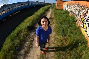 Porträt eines emotionalen jungen Mädchens mit schwarzen Haaren und Piercings. Ein Weitwinkelfoto eines Mädchens mit Aerosol-Farbdosen in den Händen auf einem Graffiti-Wandhintergrund. ein modernes Porträt eines Fisheye-Objektivs foto