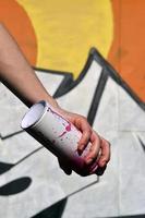 Foto der Hand eines Mädchens mit Aerosol-Farbdosen in den Händen auf einem Graffiti-Wandhintergrund. das Konzept der Straßenkunst und die Verwendung von Aerosolfarben. Graffiti-Kunstladen-Hintergrundbild