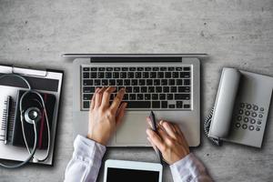 Draufsicht Tisch Arzt. Gesundheitsversorgung und medizinische Dienstleistungen mit Rundschreiben, Laptop, Tablet und Smartphone. Blick von oben auf die Hand des Medizinarztes, die mit dem Computer auf dem Schreibtisch arbeitet foto