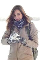 Ein junges und fröhliches kaukasisches Mädchen in einem braunen Mantel hält im Winter einen Schneeball im Hintergrund einer Horizontlinie zwischen dem Himmel und einem zugefrorenen See foto