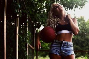 junges blondes Mädchen mit orangefarbenem Basketball posiert im Freien foto