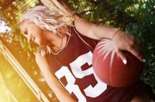 junges blondes Mädchen mit orangefarbenem Basketball posiert im Freien foto