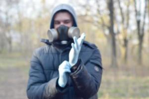 verschwommenes Porträt eines jungen Mannes in Schutzgasmaske trägt Einweghandschuhe aus Gummi im Freien im Frühlingsholz foto