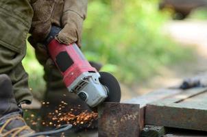 Elektrisches Radschleifen auf Stahlkonstruktion im Freien. alter arbeiter in schutzhandschuhen, der metalltür mit schleifer schneidet foto