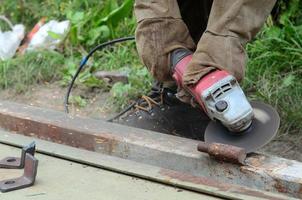 Elektrisches Radschleifen auf Stahlkonstruktion im Freien. alter arbeiter in schutzhandschuhen, der metalltür mit schleifer schneidet foto