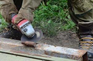 Elektrisches Radschleifen auf Stahlkonstruktion im Freien. alter arbeiter in schutzhandschuhen, der metalltür mit schleifer schneidet foto