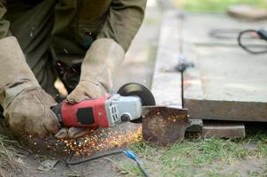 Elektrisches Radschleifen auf Stahlkonstruktion im Freien. alter arbeiter in schutzhandschuhen, der metalltür mit schleifer schneidet foto