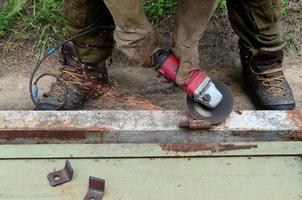 Elektrisches Radschleifen auf Stahlkonstruktion im Freien. alter arbeiter in schutzhandschuhen, der metalltür mit schleifer schneidet foto