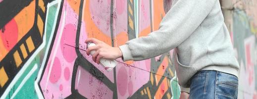 Die Hand eines jungen Mannes in einem grauen Hoodie malt Graffiti in Pink und foto