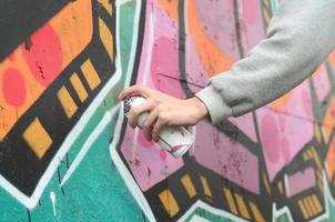 ein junger Mann in einem grauen Hoodie malt Graffiti in Pink und Grün c foto
