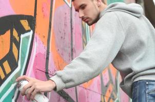 ein junger Mann in einem grauen Hoodie malt Graffiti in Pink und Grün c foto