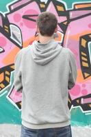 Ein junger Graffiti-Künstler in einem grauen Hoodie blickt mit auf die Wand foto