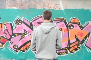 Ein junger Graffiti-Künstler in einem grauen Hoodie blickt mit auf die Wand foto