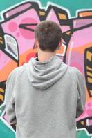 Ein junger Graffiti-Künstler in einem grauen Hoodie blickt mit auf die Wand foto