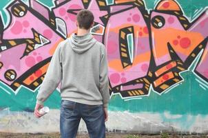 Ein junger Graffiti-Künstler in einem grauen Hoodie blickt mit auf die Wand foto