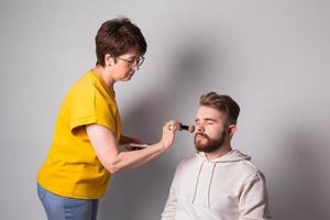 bärtiger mann, der sich schminkt. Frau Visagist arbeitet mit Pinsel. foto