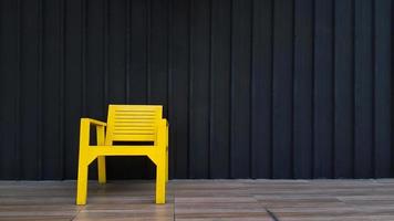 Gelber Holzstuhl auf braunem Fliesenboden mit schwarzer Rollladenwand für Hintergrund und Kopierfläche rechts. Objekt zum Platz nehmen mit dunkler Edelstahltapete. foto
