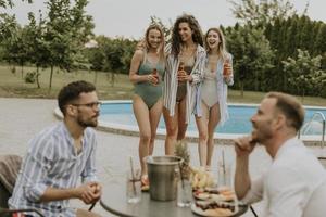 Gruppe junger Leute, die mit Getränken jubeln und Obst am Pool im Garten essen foto