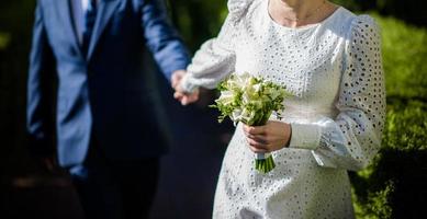 Die Braut in einem weißen Hochzeitskleid hält einen Strauß weißer Blumen - Pfingstrosen, Rosen. Hochzeit. Braut und Bräutigam. zarter Willkommensstrauß. schöne Dekoration von Hochzeiten mit Blättern foto