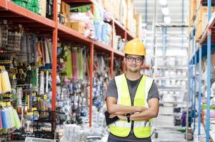 intelligenter asiatischer ingenieur männlicher arbeiter mit schutzhelm, der den bestand an haushaltswaren in den regalen im lagerhaus, in der fabrik verwaltet. foto