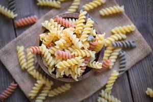 Nudeln rohe Makkaroni auf Holzschüssel Hintergrund, Nahaufnahme rohe Makkaroni Spiralnudeln ungekochte köstliche Vollkorn-Fusilli-Nudeln zum Kochen von Speisen foto