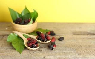 frisches Obst - Maulbeere mit Blatt auf Holztisch vor gelbem Hintergrund foto