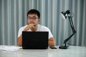 lächelnder asiatischer freiberuflicher mann, der an einem laptop in einer modernen bürolobby arbeitet. junger indischer Student, der Computer-Fernstudium verwendet, Online-Webinar anschaut, virtuelles Training bei Videoanrufen foto