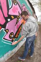 ein junger Mann in einem grauen Hoodie malt Graffiti in Pink und Grün c foto