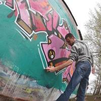 ein junger Mann in einem grauen Hoodie malt Graffiti in Pink und Grün c foto