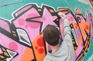 ein junger Mann in einem grauen Hoodie malt Graffiti in Pink und Grün c foto