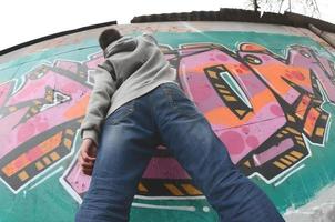 ein junger Mann in einem grauen Hoodie malt Graffiti in Pink und Grün c foto