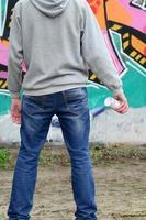 Ein junger Graffiti-Künstler in einem grauen Hoodie blickt mit auf die Wand foto