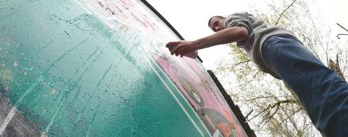 ein junger Mann in einem grauen Hoodie malt Graffiti in Pink und Grün c foto