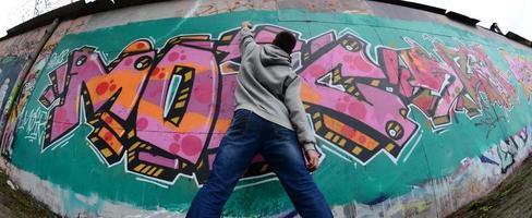 ein junger Mann in einem grauen Hoodie malt Graffiti in Pink und Grün c foto