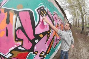 ein junger Mann in einem grauen Hoodie malt Graffiti in Pink und Grün c foto