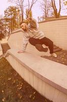 ein junger Mann macht einen Sprung durch die Betonbrüstung. Der Athlet übt Parkour und trainiert unter Straßenbedingungen. das Konzept der sportlichen Subkulturen unter Jugendlichen foto